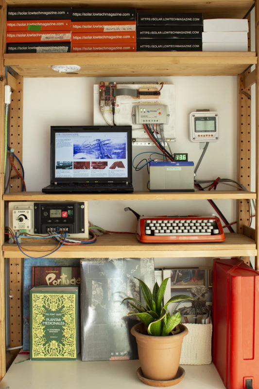 The solar powered server in its new housing, screwed against the wall in the living room. The battery is in front. The solar charge controller below the laptop powers the lights in the room. Image by Marie Verdeil.