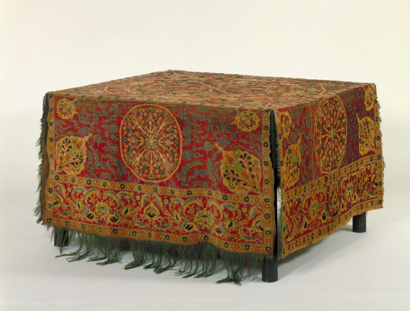 Image: Table carpet woven in cruciform shape, wool knotted pile on wool foundation, medallion design with Ottoman floral motifs on red ground, probably Ottoman Cairo, Egypt, 1550-1600. Source: V&A. https://collections.vam.ac.uk/item/O67146/table-carpet-table-carpet-unknown/