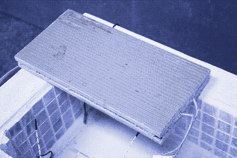 Image: A removable heat brick, consisting of a nichrome circuit sandwiched between two identical tiles. It rests upon an insulated solar electric cooking device. Photo by Marie Verdeil.